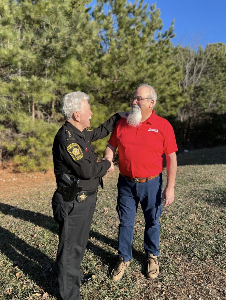 Sheriff Harris and Rich standing in front of trees shaking hands